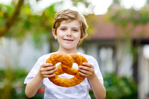 Adorável menino pequeno comendo enorme grande bávaro alemão pretzel. — Fotografia de Stock