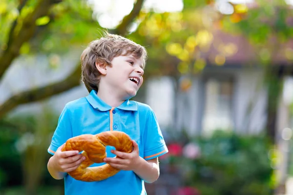 Adorável menino pequeno comendo enorme grande bávaro alemão pretzel. — Fotografia de Stock