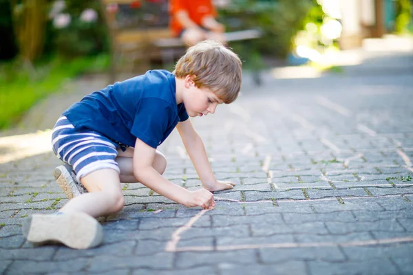 Pequeño chico rubio divertido jugando al hopscotch en el patio al aire libre — Foto de Stock