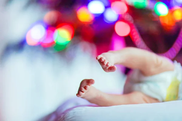 Bebé recién nacido pies y pañal con árbol de Navidad y luces de guirnalda de colores — Foto de Stock