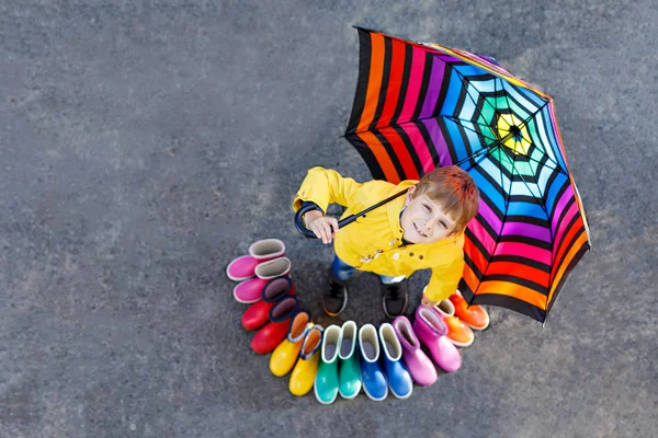 Ragazzino e gruppo di stivali da pioggia colorati. Biondo bambino in piedi sotto l'ombrello . — Foto Stock