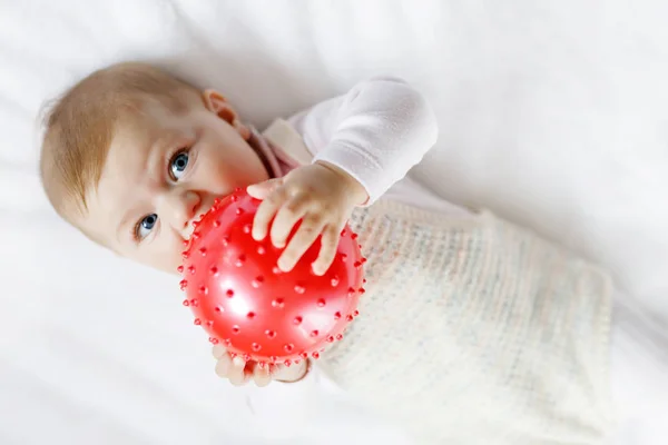 Tatlı bebek kırmızı sakız topuyla oynuyor, sürünüyor, kavrıyor — Stok fotoğraf
