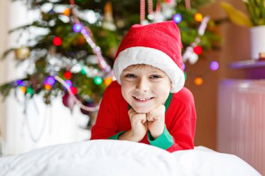 Noel ağacı ve arka plan ışığı ile Noel Baba şapkalı küçük çocuk çocuk.