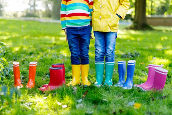 Małe dzieci, chłopców i dziewczyny w dżinsy i żółtą kurtkę w kolorowy deszcz buty — Zdjęcie stockowe