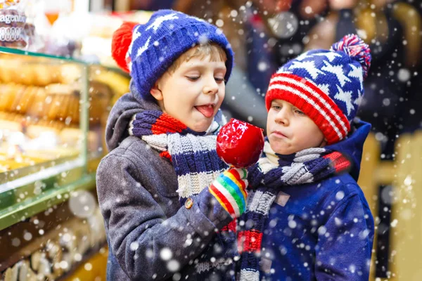 Dos niños pequeños comiendo azúcar manzana dulces de pie en el mercado de Navidad — Foto de Stock