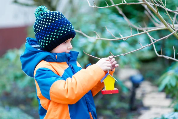 Little kid boy hanging bird house on tree for feeding in winter — Stock Photo, Image
