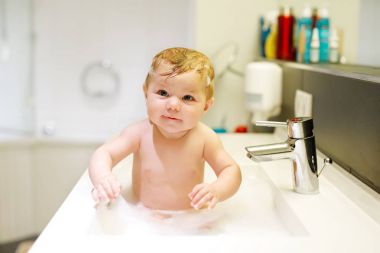 Lavaboda yıkanan, su ve köpükle oynayan sevimli bir bebek.