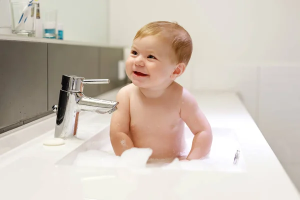 Bebê adorável bonito tomando banho na pia de lavagem e brincando com água e espuma — Fotografia de Stock