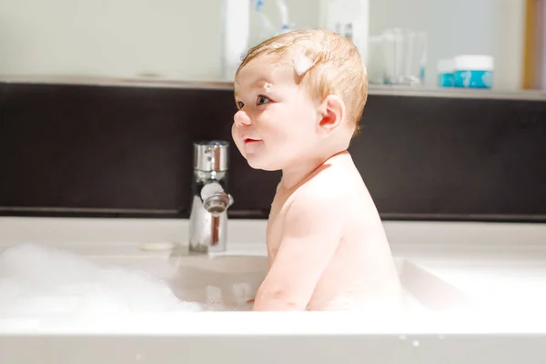 Bebê adorável bonito tomando banho na pia de lavagem e brincando com água e espuma — Fotografia de Stock