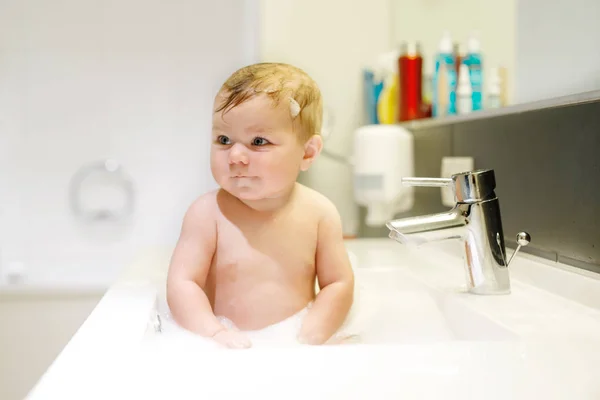 Roztomilé roztomilé dítě se koupe v umyvadle a hraje si s vodou a pěnou — Stock fotografie