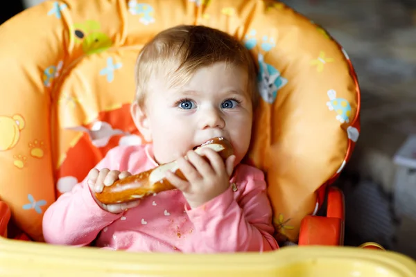 Cute little baby girl eating bread. Child eating for the first time piece of pretzel. — Stock Photo, Image