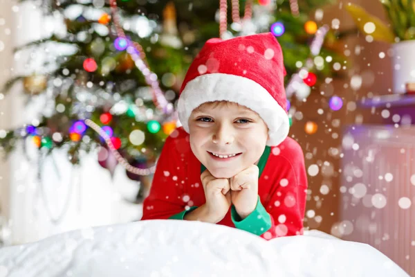 Liten unge pojke i Tomtemössa med julgran och lamporna på bakgrunden. — Stockfoto