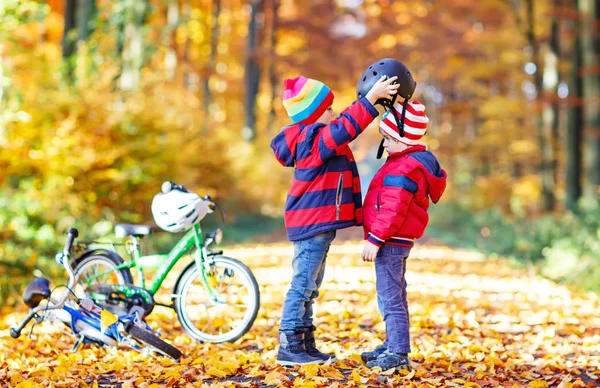 Dois garotinhos com bicicletas na floresta de outono colocando capacetes — Fotografia de Stock