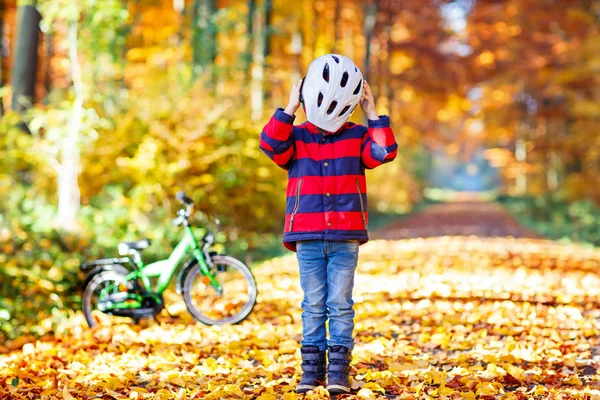 Criança ativa colocando capacete seguro antes de andar de bicicleta no dia ensolarado de outono na natureza. — Fotografia de Stock