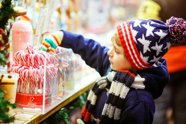 Kleine schattige jongen jongen kopen snoep uit een cancy staan op de kerstmarkt — Stockfoto