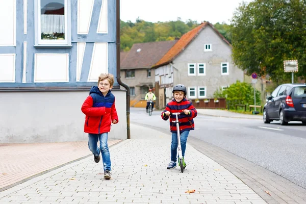 Dos niños pequeños de la escuela corriendo y conduciendo en scooter en el día de otoño —  Fotos de Stock