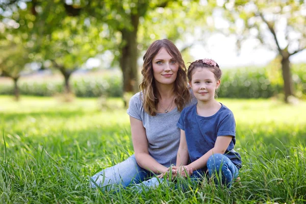 Belle jeune mère et petite fille assise sur l'herbe verte et au repos — Photo