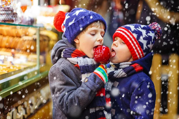 2 小さな子供男の子砂糖のリンゴのお菓子を食べてクリスマス マーケットの上に立つ — ストック写真
