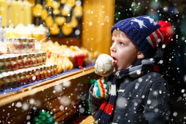 Petit garçon mangeant du sucre pomme bonbons stand sur le marché de Noël — Photo