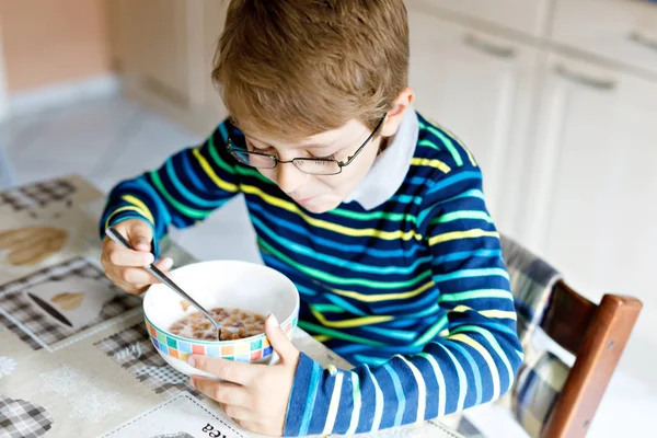 Счастливый маленький блондин, который ест хлопья на завтрак или обед. Здоровое питание для детей . — стоковое фото