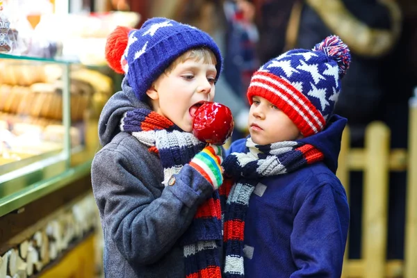 Two little kid boys eating sugar apple sweets stand on Christmas market — Stock Photo, Image