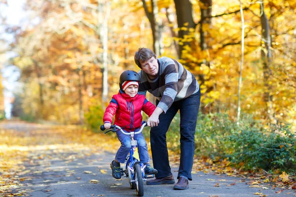 Liten pojke och hans far i höstparken med cykel. Pappa lär sin son cykla — Stockfoto