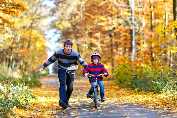 Ragazzino e suo padre nel parco autunnale in bicicletta. Papà insegnare a suo figlio in bicicletta — Foto Stock