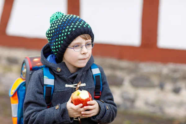 Little kid boy with eye glasses walking from the school and eating apple — Stock Photo, Image