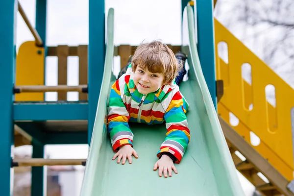 Felice ragazzo biondo che si diverte e scivola sul parco giochi all'aperto — Foto Stock