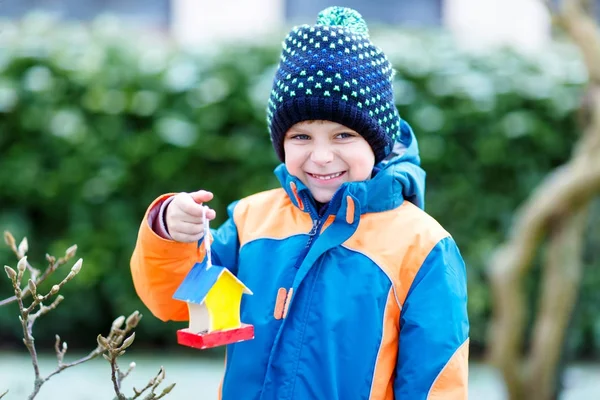 Little kid boy hanging bird house on tree for feeding in winter — Stock Photo, Image