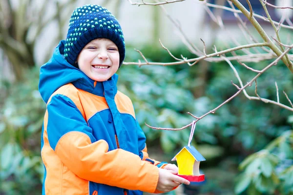 Little kid boy hanging bird house on tree for feeding in winter — Stock Photo, Image