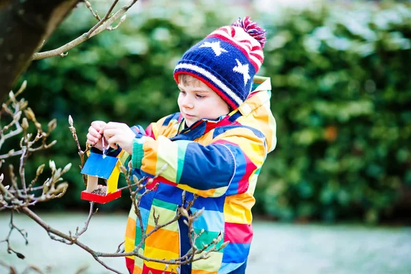 Little kid boy hanging bird house on tree for feeding in winter — Stock Photo, Image