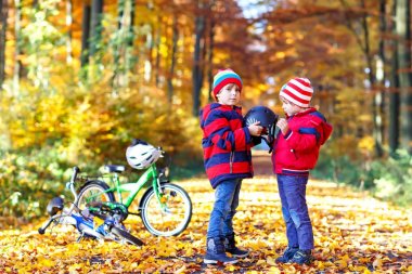 İki küçük çocuklar kask koyarak sonbahar ormandaki bisiklet ile çocuk