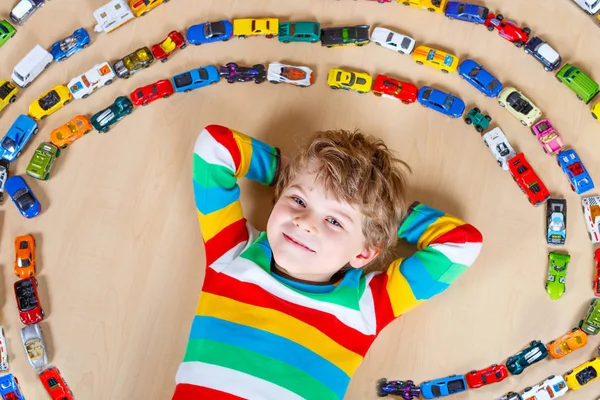 Lindo niño rubio pequeño jugando con un montón de coches de juguete interior . — Foto de Stock