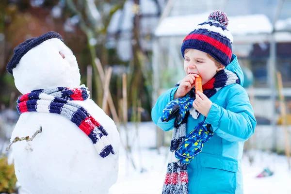 Chico gracioso haciendo un muñeco de nieve en invierno al aire libre — Foto de Stock