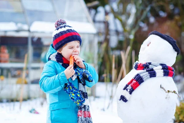 Funny kid boy making a snowman in winter outdoors — Stock Photo, Image