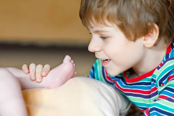 Little kid boy kissing and playing with foot of newborn baby. — Stock Photo, Image