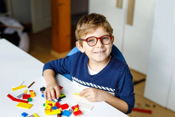 Niño rubio con anteojos jugando con muchos bloques de plástico de colores . — Foto de Stock