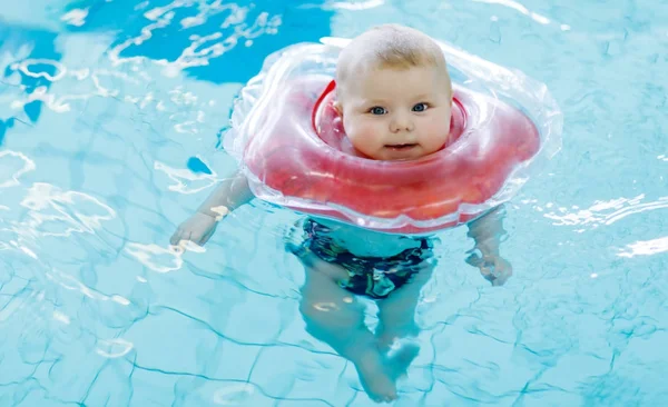 Lindo bebé pequeño aprendiendo a nadar con anillo de natación en una piscina cubierta — Foto de Stock