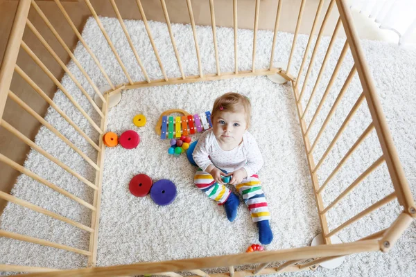 Mooie babymeisje zit in de kinderbox. Leuk schattig kind spelen met kleurrijke speelgoed — Stockfoto