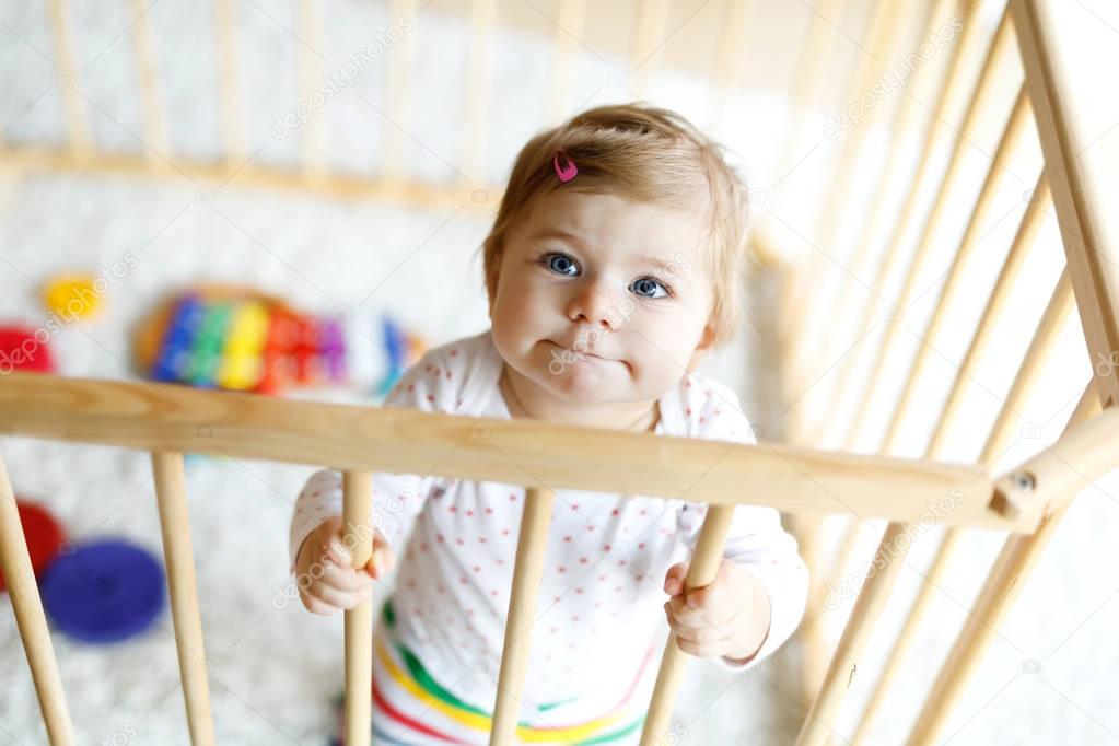 Beautiful little baby girl standing inside playpen. Cute adorable child playing with colorful toy