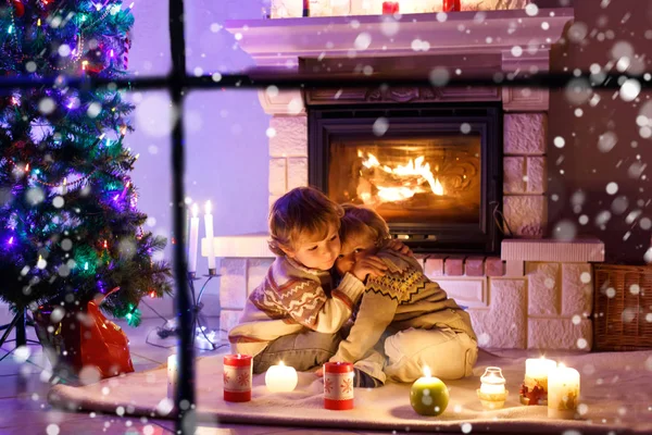 Cute toddler boys, blond twins playing together and lookinig on fire in chimney. Family celebrating xmas holiday