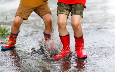 İki çocuk kırmızı giyen bir su birikintisi içine atlama botlar yağmur.