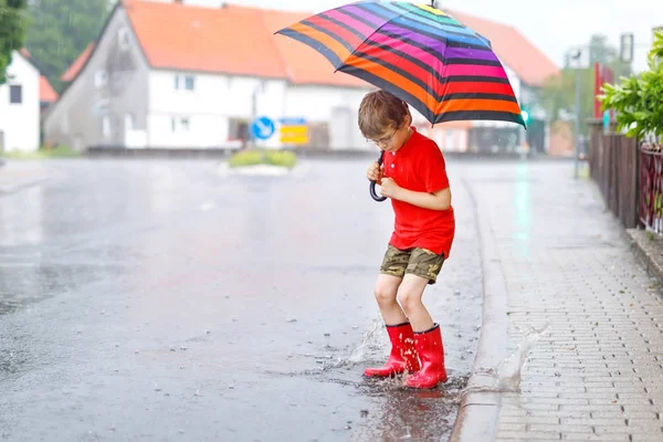 Kid boy vestindo botas de chuva vermelha e andando com guarda-chuva — Fotografia de Stock