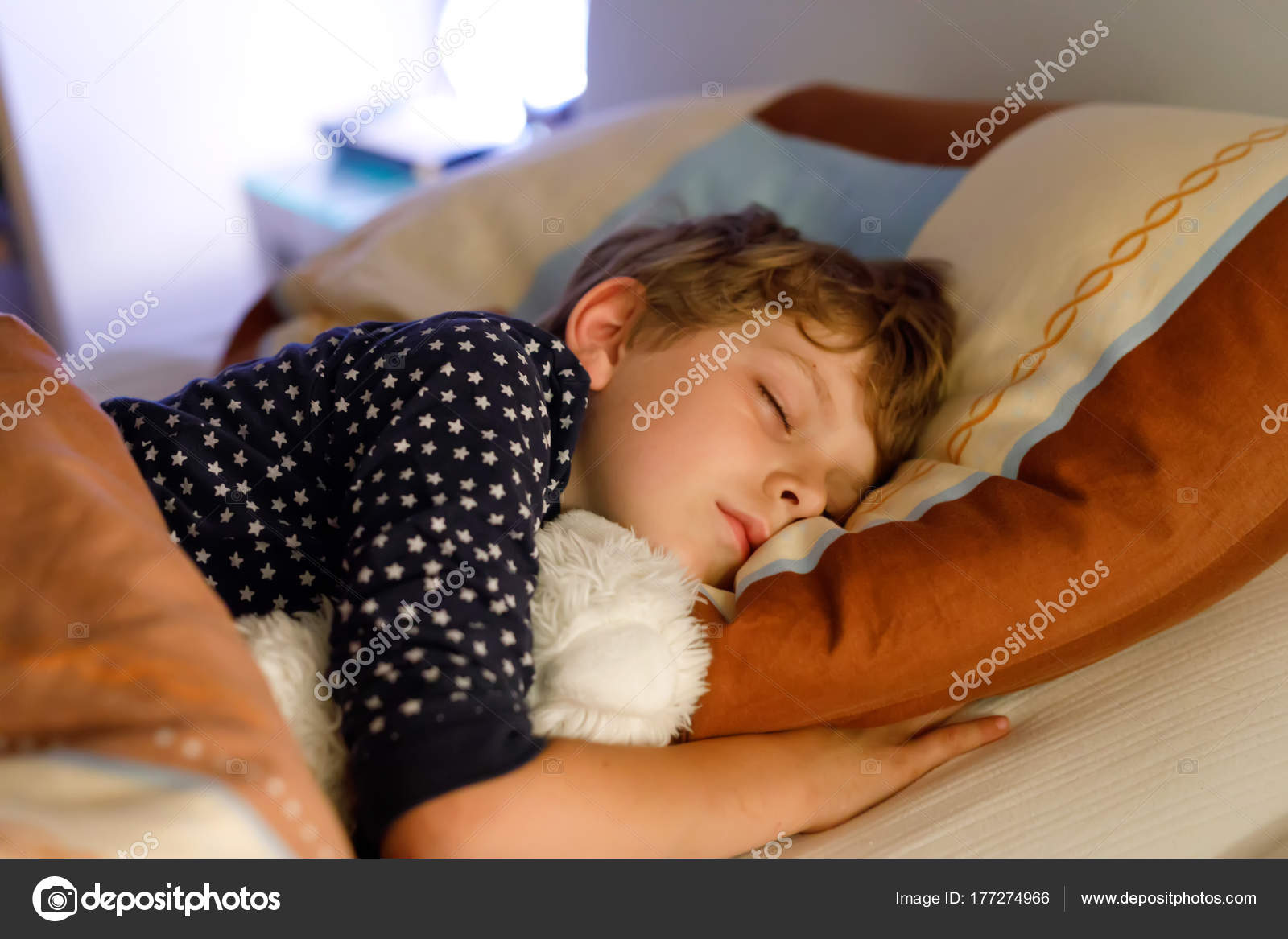 Little preschool kid boy sleeping in bed with colorful lamp. Stock