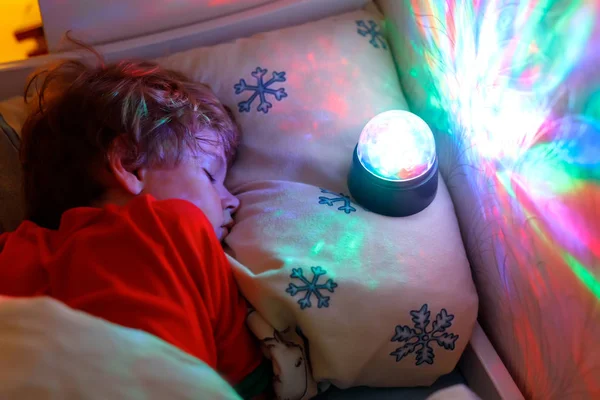 Pequeño niño preescolar durmiendo en la cama con lámpara de colores . — Foto de Stock