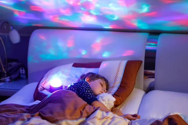 Pequeno menino pré-escolar dormindo na cama com lâmpada colorida . — Fotografia de Stock