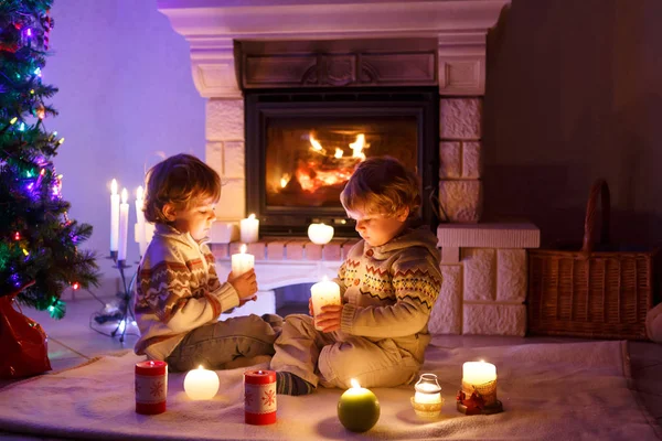 Lindos niños pequeños, gemelos rubios jugando juntos y mirando al fuego en la chimenea. Familia celebrando la fiesta de Navidad — Foto de Stock