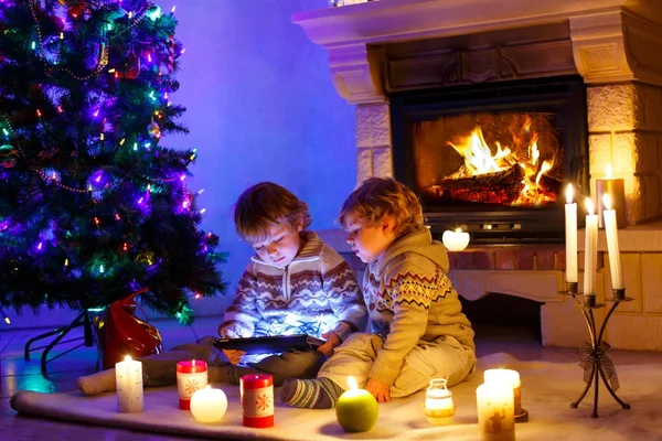 Zwei niedliche Kleinkinder, blonde Zwillinge, die mit einem neuen Tablet-Geschenk spielen. Familie feiert Weihnachtsfest — Stockfoto