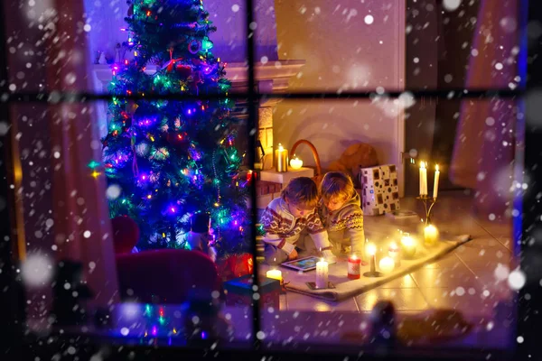 Dos niños pequeños sentados junto a una chimenea en casa en Navidad — Foto de Stock